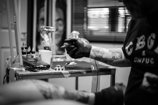black and white image of a person holding a tattoo needle inside a tattoo studio